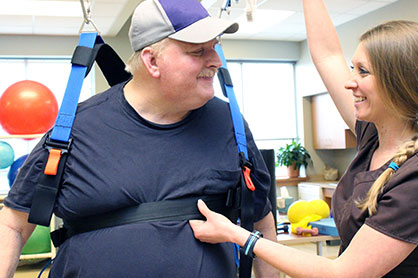 A male patient being secured in a harness by a therapist.