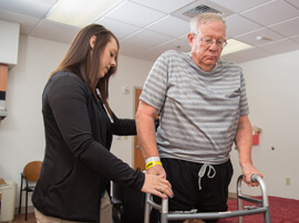 Therapist supporting elderly male using walker